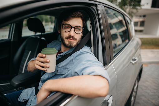 Young casual business man driving car and drinking coffee on the way to work