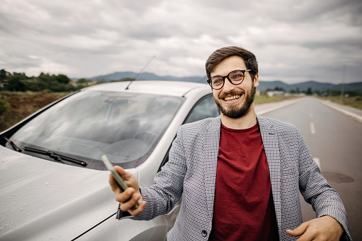 Young man using phone in front of the car