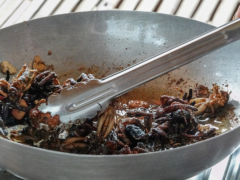 Large crickets and tarantulas being fried in a pan.