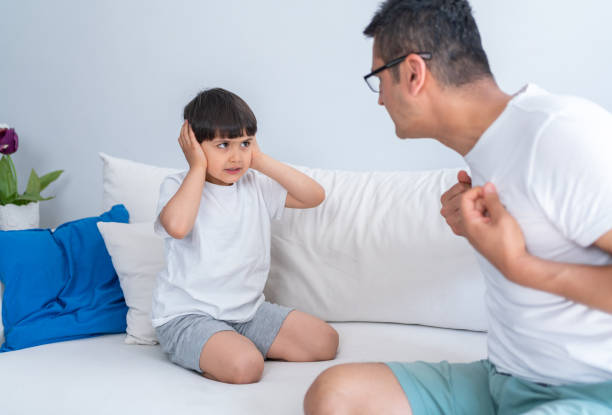 istock Irritated Father Shouting At Unhappy Little Son While He Covering Ears Sitting On Sofa At Home. Angry strict father shouting screaming at little son. 1321311469
