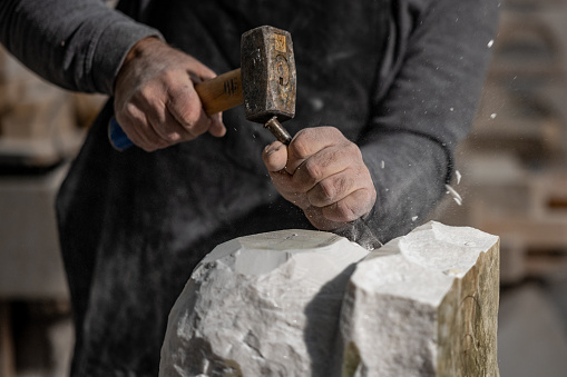 Stonemason carving a sculpture with chisel and hammer in the workshop.