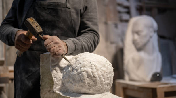 Mid section of stonemason carving a sculpture with chisel and hammer in the workshop.