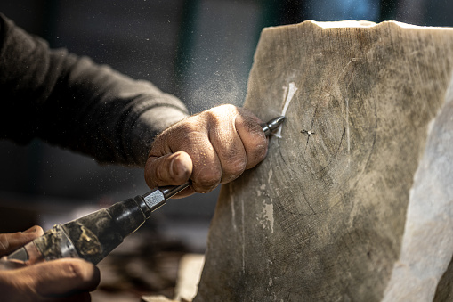 Close-up of stonemason's hands chiselling on piece of stone using chisel.