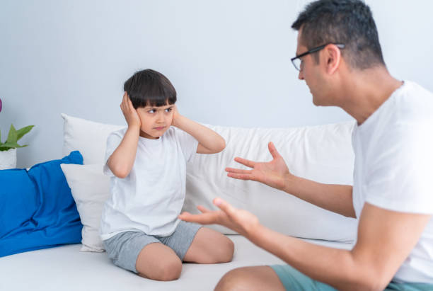 istock Irritated Father Shouting At Unhappy Little Son While He Covering Ears Sitting On Sofa At Home. Angry strict father shouting screaming at little son. 1321311706