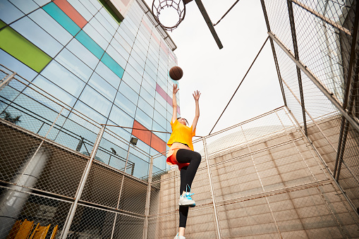 young asian woman playing basketball making a shot on outdoor court