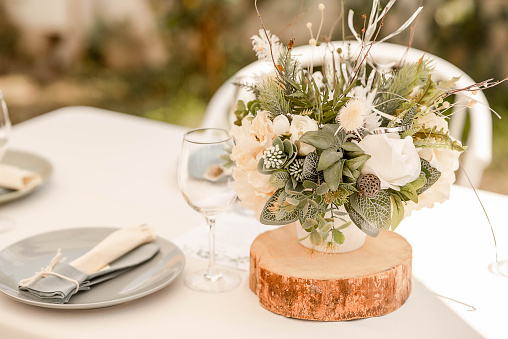 Table arrangement with natural rustic notes featuring herbal floral centerpieces, soft linen table cloth and pastel details, elegant setup for guests at a wedding reception, restaurant or at a party.
