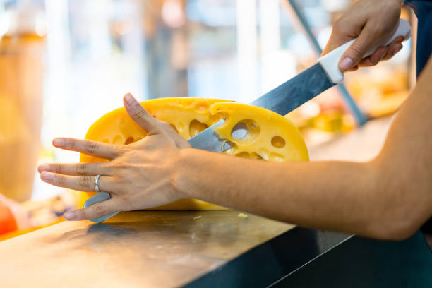 Cropped image of employee cutting cheese at counter. Female owner is working in delicatessen. She is in store.