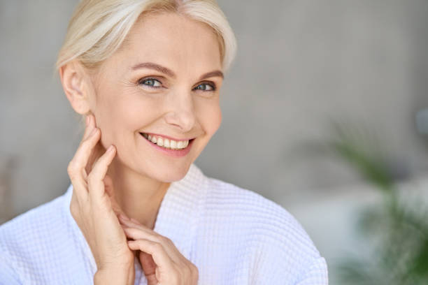 Portrait of smiling mid age woman looking at camera. Skin care concept. Closeup of happy smiling beautiful middle aged woman spa salon client wearing bathrobe looking at camera touching face. Spa procedures advertising. Skin care products concept. Copy space. antiaging stock pictures, royalty-free photos & images