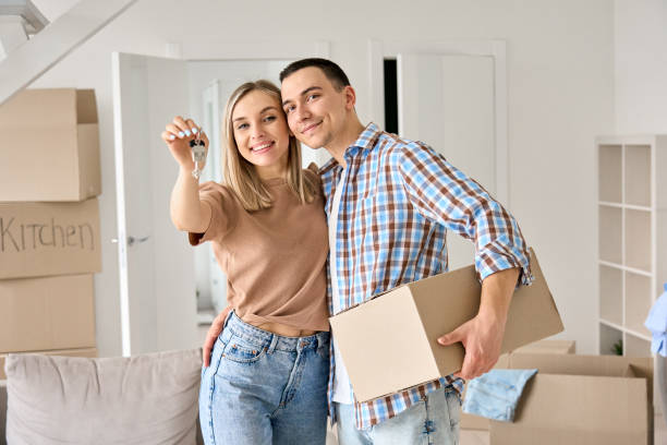 Happy young couple first time home owners holding keys in new home. Happy young couple home owners holding keys in new home. Smiling independent millennial man and woman first time homeowners carrying boxes on moving day. Mortgage loan, new house ownership concept. happy family with key of their new house stock pictures, royalty-free photos & images