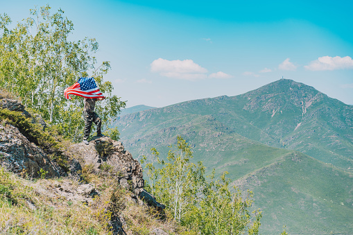 On rock, man in military uniform holding an American flag.