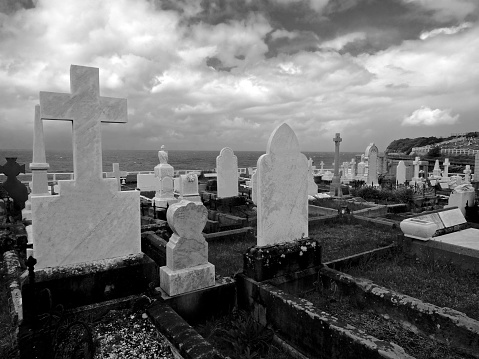 Black and white photography of unidentifiable gravestones by the seaside