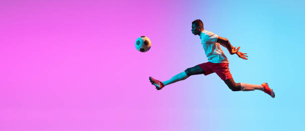istock Flyer. One African man, professional soccer football player training isolated on gradient blue pink background in neon light. 1321328030