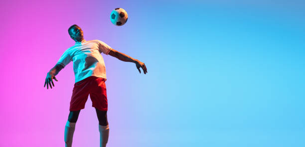 istock Flyer. One African man, professional soccer football player training isolated on gradient blue pink background in neon light. 1321328039