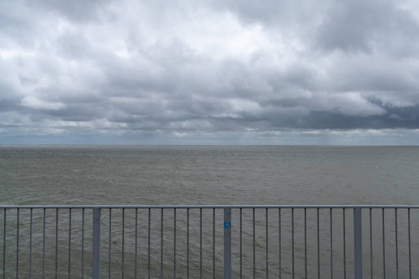 Landscape of expressive cloudy and overcast sky over a windbeaten Wadden Sea in the Netherlands with a guard rail in the foreground