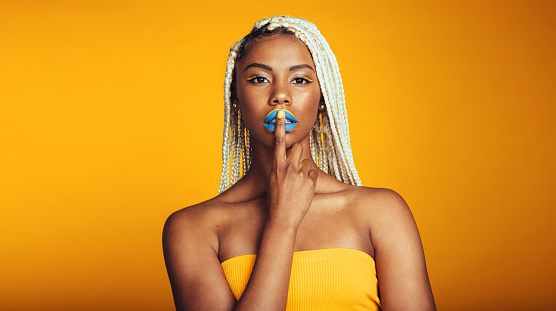 Close up of woman with painted lips on yellow background. Portrait of artistic african american woman with braided hair showing shh.