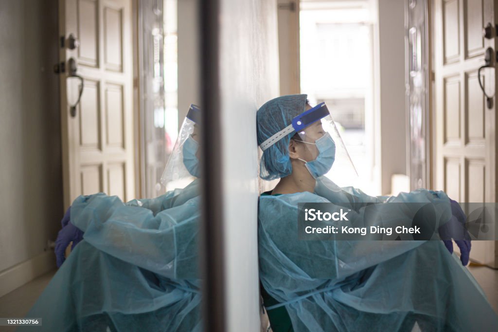 Asian Chinese female front liner tired sitting on floor during Pandemic Nurse Stock Photo