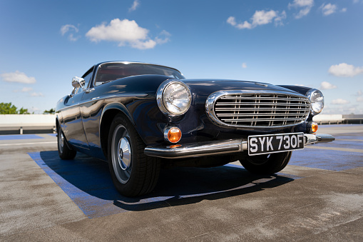 Hertfordshire - May 27, 2021: The sun shines down on a dark blue Volvo 1800S from 1967 in a car park.