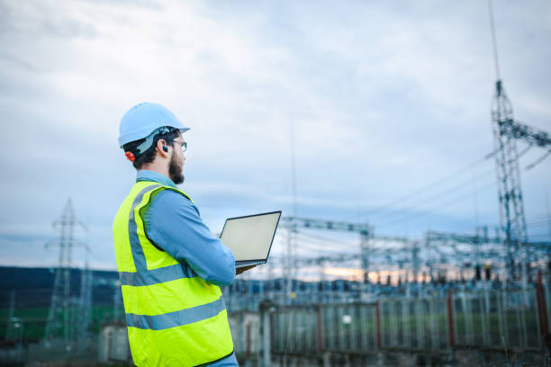 istock Electrical engineer working on a laptop in front of Electricity power station 1321331334