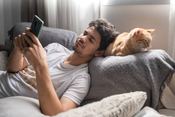 istock young man lays his head on the back of a brown tabby cat lying on the sofa, while using his cellphone 1321331360