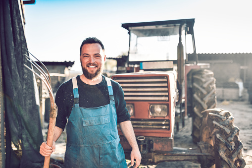 Smiling Male Farmer Enjoying Working With Tractor And Pitchfork