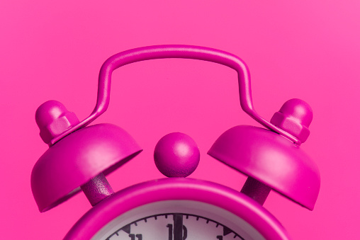 Close-up of pink alarm clock on pink background.