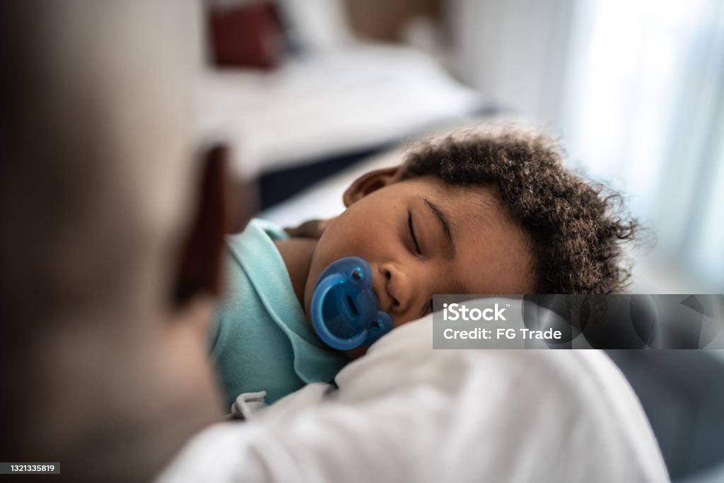 Father putting baby son to sleep on his arms at home Mature father putting baby son to sleep on his arms at home Baby - Human Age Stock Photo