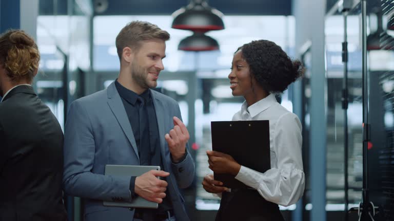 Multiracial couple having discussion in corridor. Colleagues waiting for meetup