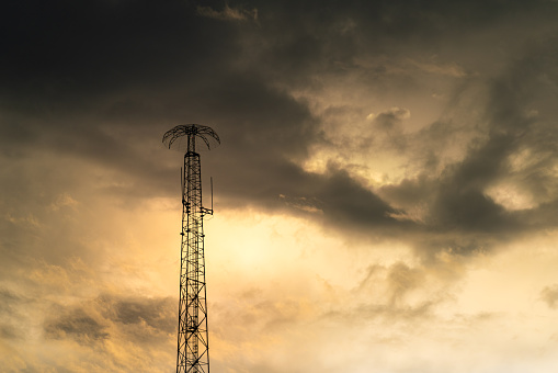 Silhouette shadow of the signal telecommunication structure pole on dramatic orange sunlight and cloudy sky background. Technology and telecommunication object photo.