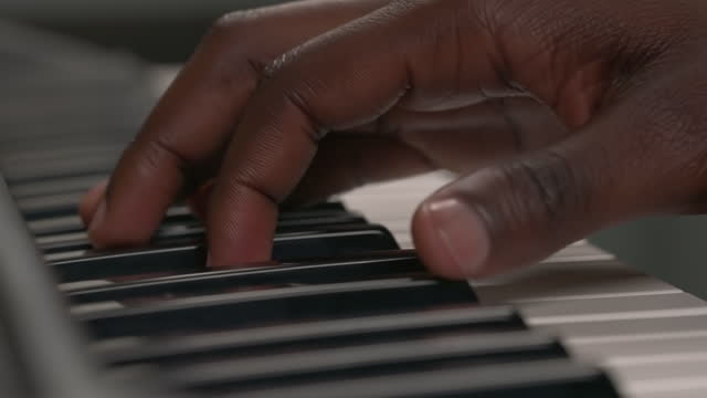 Macro shot of African American male's hand pressing notes on musical keyboard. Practicing solo music on piano or synthesizer. Learning to play piano