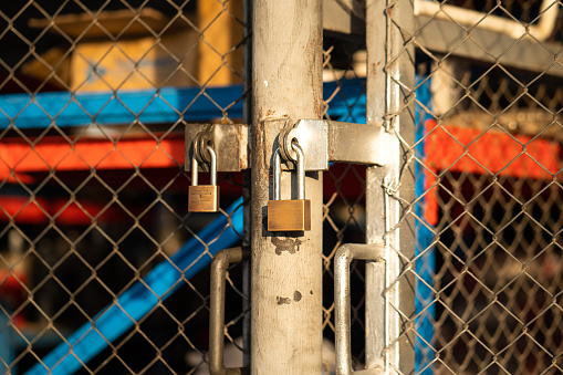 A heavy duty used steel padlock is locking on sliding metal gate of the warehouse storage, restriced area.