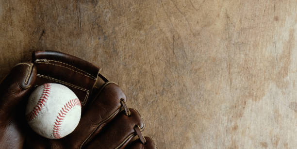 baseball ball and glove on wooden background Old rustic sports background with top view of vintage glove holding ball on wood backdrop. baseballs stock pictures, royalty-free photos & images