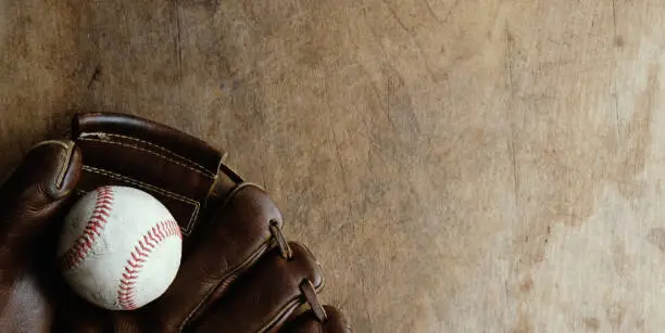 Old rustic sports background with top view of vintage glove holding ball on wood backdrop.