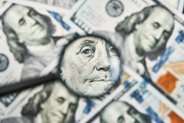 istock Magnifying glass on a pile of 100 dollar banknotes 1321359736