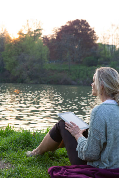 istock Woman relaxes in meadow with digital tablet, above river 1321365784
