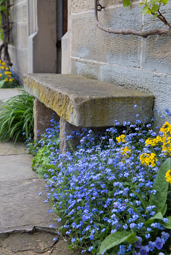 Old rural stone bench with flowers outside a farm house