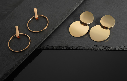 Modern golden earrings collection on dark stone background with copy space