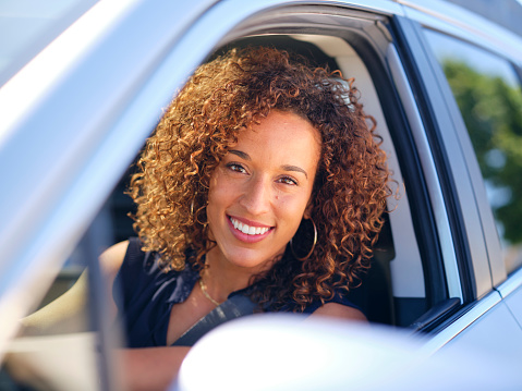 A happy mixed ethnicity woman driving a car.