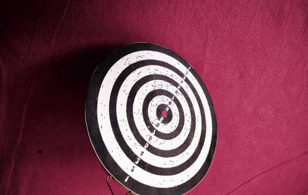 already used and secondhand dart board standing on red carpet on ground and with its shadows. - eyes narrowed imagens e fotografias de stock