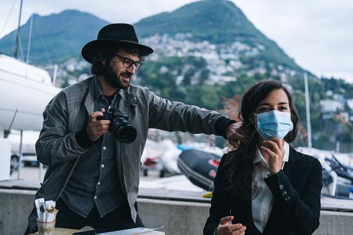 Man photographs her as she enjoys breakfast before work, coastline of Lake Lugano behind