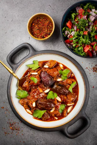Traditional Moroccan lamb tagine simmered in spices, with dates and almonds. Salad and spices. Grey background. Vertical image.