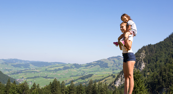 Happy mom and child hiking outdoors in the mountains looking at the countryside scenery.