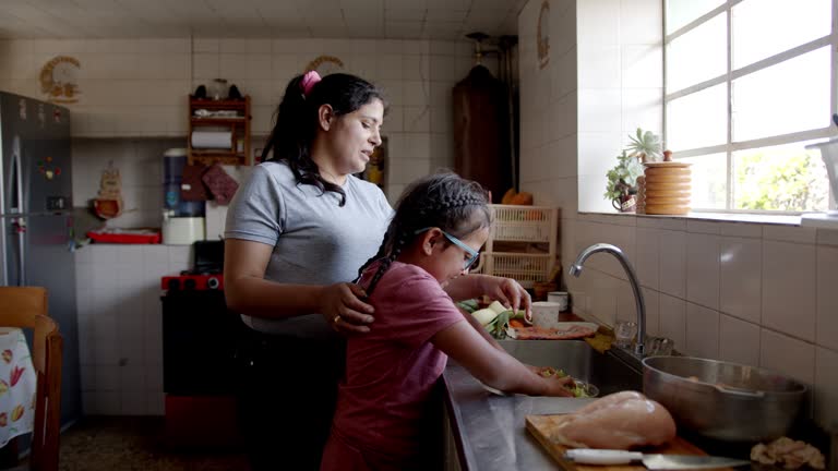 Latin American mother teaching her daughter to cook dinner at home - lifestyle concepts