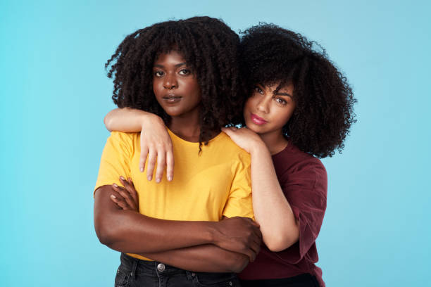 Studio shot of two young women embracing each other against a blue background She's more like a sister to me lgbtqcollection stock pictures, royalty-free photos & images