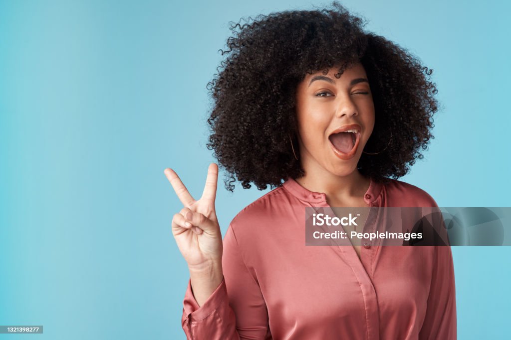 Studio shot of an attractive young woman making a peace gesture against a blue background Love and peace to all my peeps Peace Sign - Gesture Stock Photo