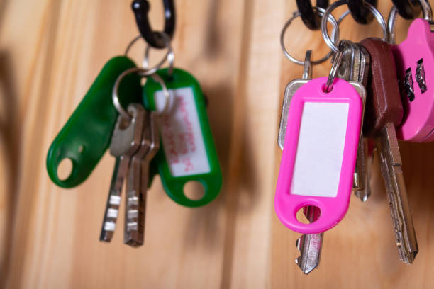 Pink keychain with copy space and keys on hooks in hallway. Wooden wall as backdrop. Many other keychains around. Low depth of field.