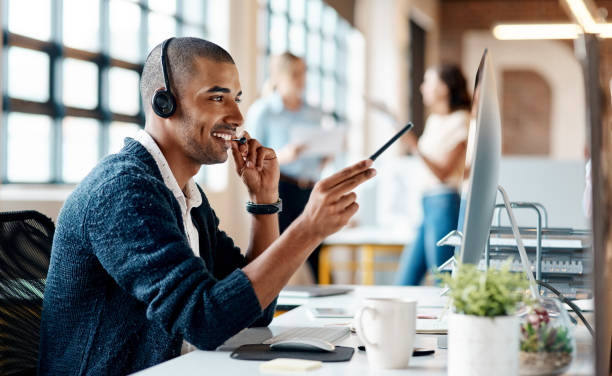 Shot of a young man using a headset and computer in a modern office