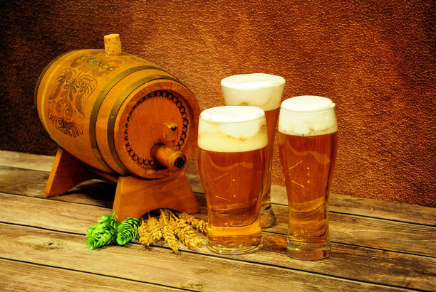 木製の樽、茶色の壁に対する木製のテーブルの上に軽いビール、ホップと小麦の耳の3つの異なるグラス。 - mug beer barley wheat ストックフォトと画像