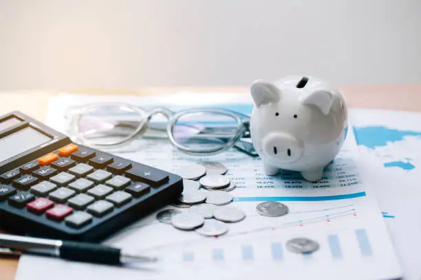 Photo of Calculator with text Tax Saving. Calculator, Piggy Bank, coins, business graph and pen on wooden table.