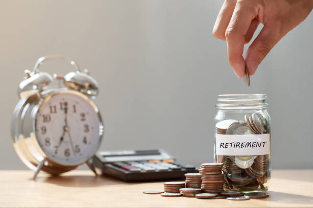 Hand putting Coins in glass jar with calculator and alarm clock for time to money saving for retirement concept ,  retirement planning. Hand putting Coins in glass jar with calculator and alarm clock for time to money saving for retirement concept ,  retirement planning. conspiracy stock pictures, royalty-free photos & images