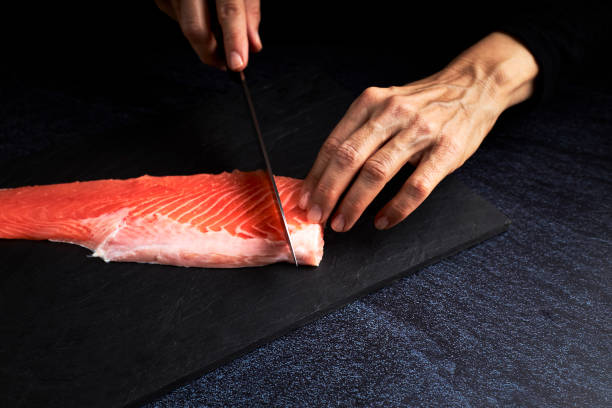 칠판에 초밥을 만들기 위해 연어 조각을 준비하는 여성 요리사. 아시아 음식 컨셉 - prepared fish 뉴스 사진 이미지